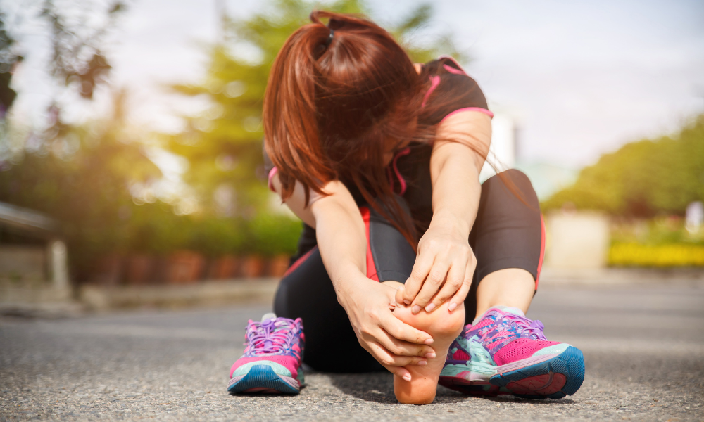 A woman sitting on a road massaging away her foot pain.