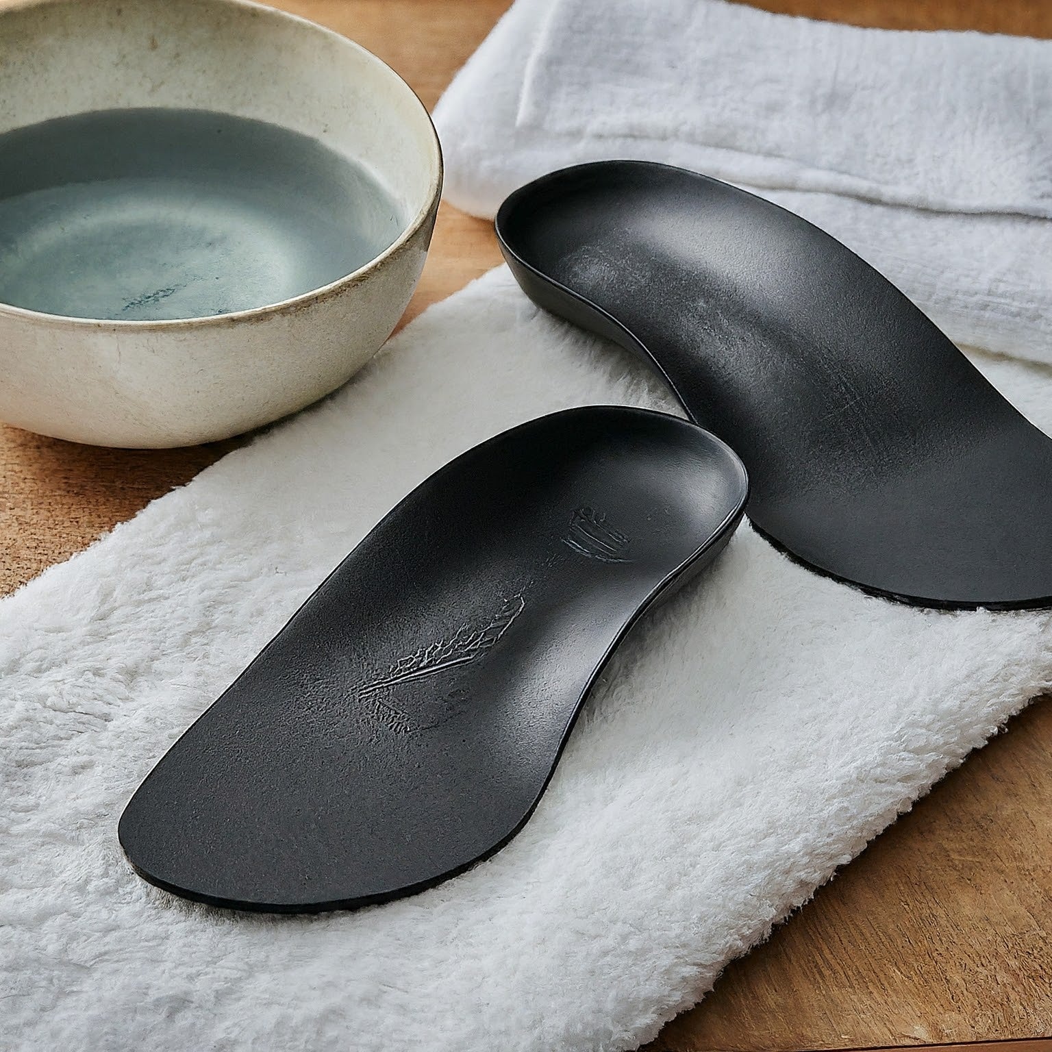 a pair of orthotics laying on a white towel next to a bowl of water