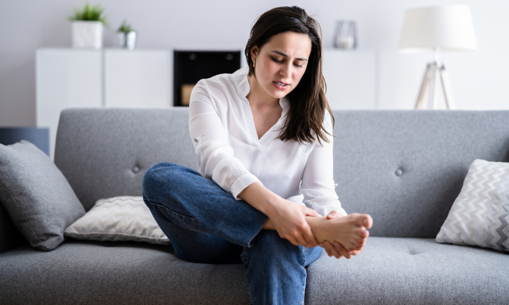 A woman is massaging her foot wondering how to get rid of calluses on feet.