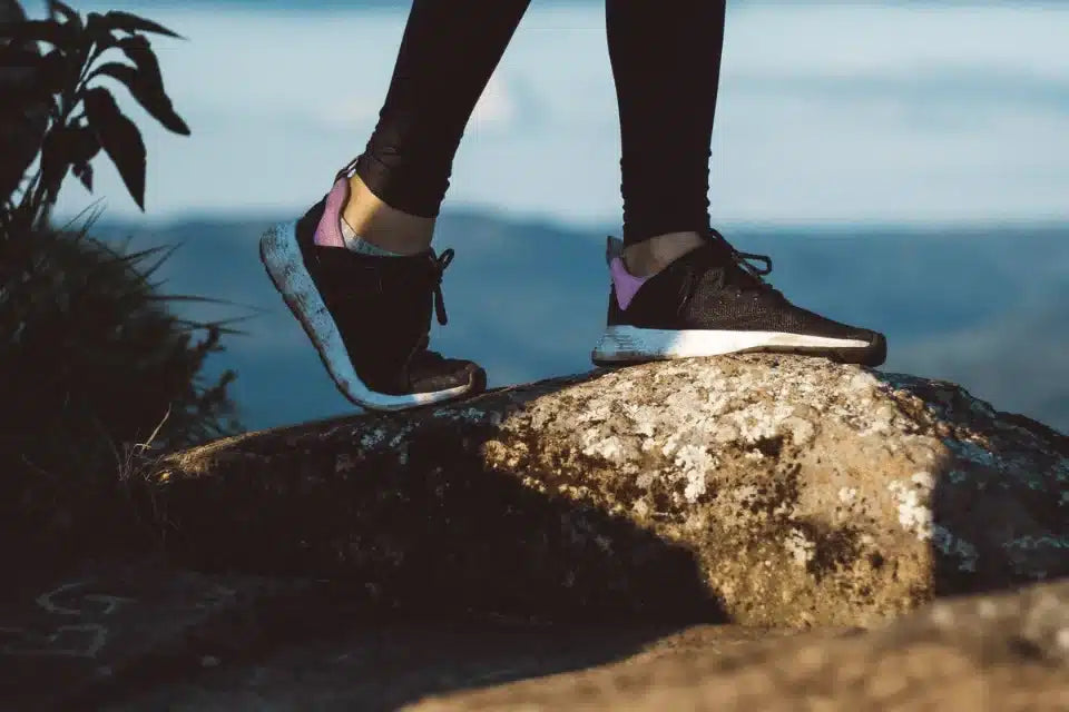 Woman standing on a rock at the top of a mountain with sudden ankle pain.